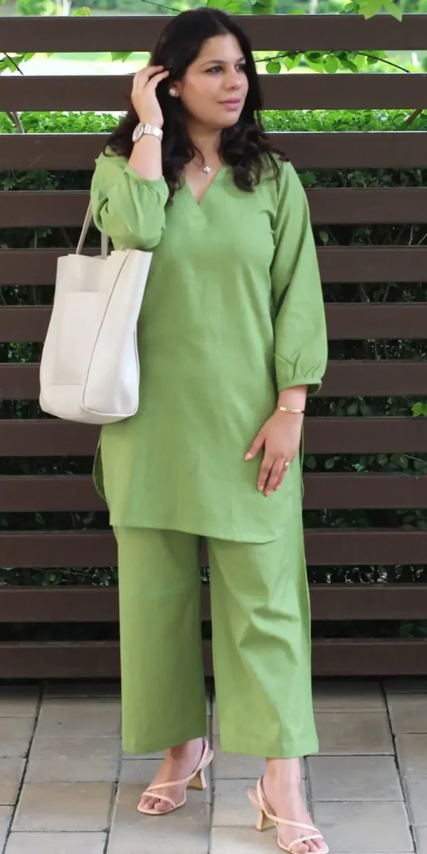 Woman wearing a sage green cotton slub tunic and wide-leg trousers set with a white tote bag. 👜