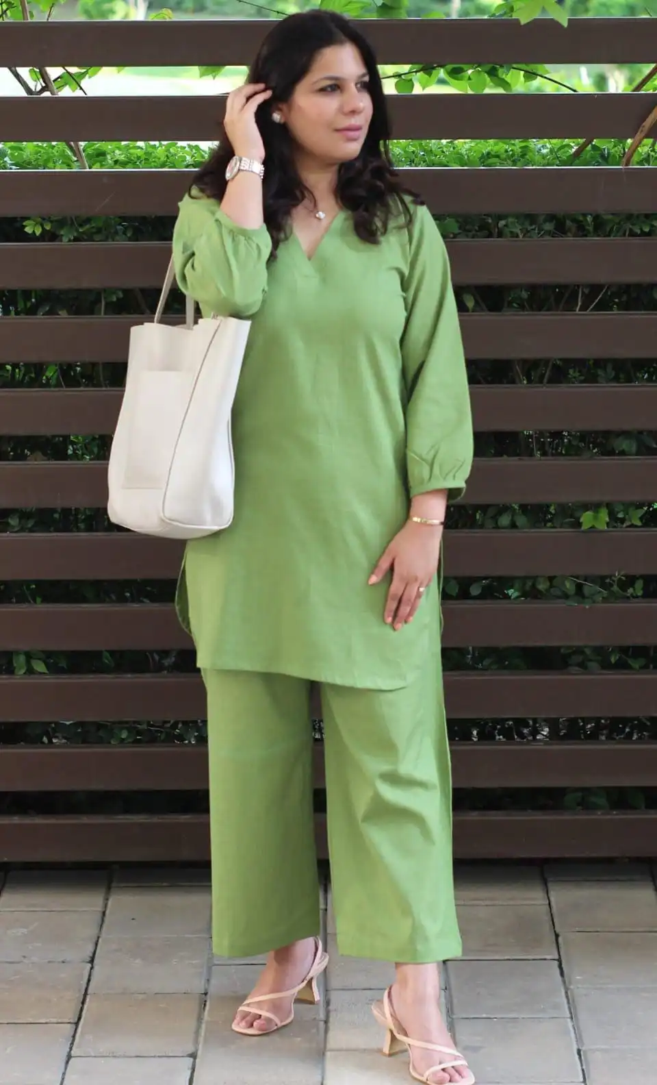 Woman wearing a sage green cotton slub tunic and wide-leg trousers set with a white tote bag. 👜