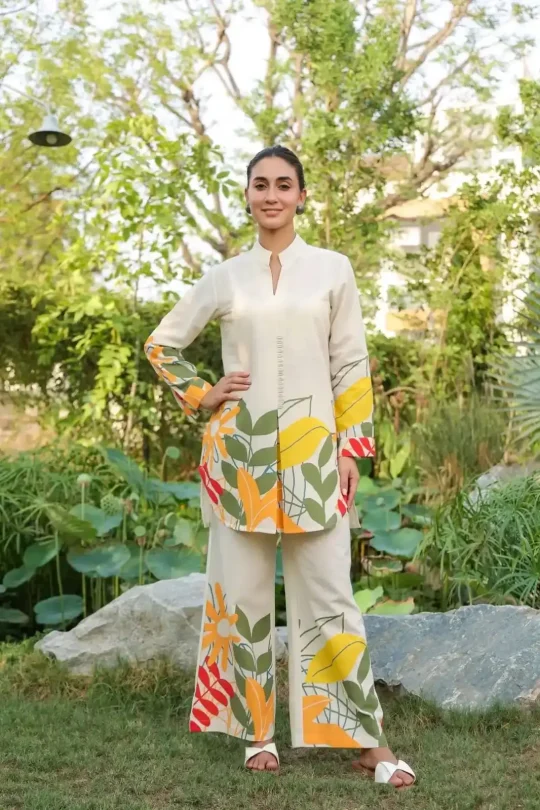 Woman wearing a cream-colored cotton flex co-ord set with vibrant yellow, orange, and green tropical leaf prints on the hem and sleeves.